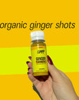Hand holding a Slapp Ginger Turmeric organic wellness shot bottle with bold yellow background and text that reads - organic ginger shots.