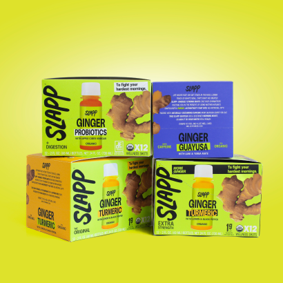 Four brightly colored boxes of SLAPP ginger wellness shots arranged against a yellow background. Variants include Ginger Probiotics, Ginger Guayusa, Ginger Turmeric Original, and Ginger Turmeric Extra Strength