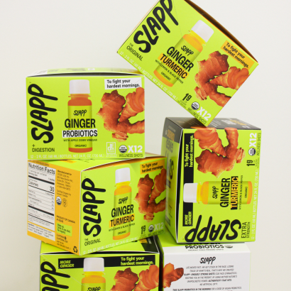 Stack of SLAPP wellness shot boxes, including Ginger Probiotics and Ginger Turmeric flavours.