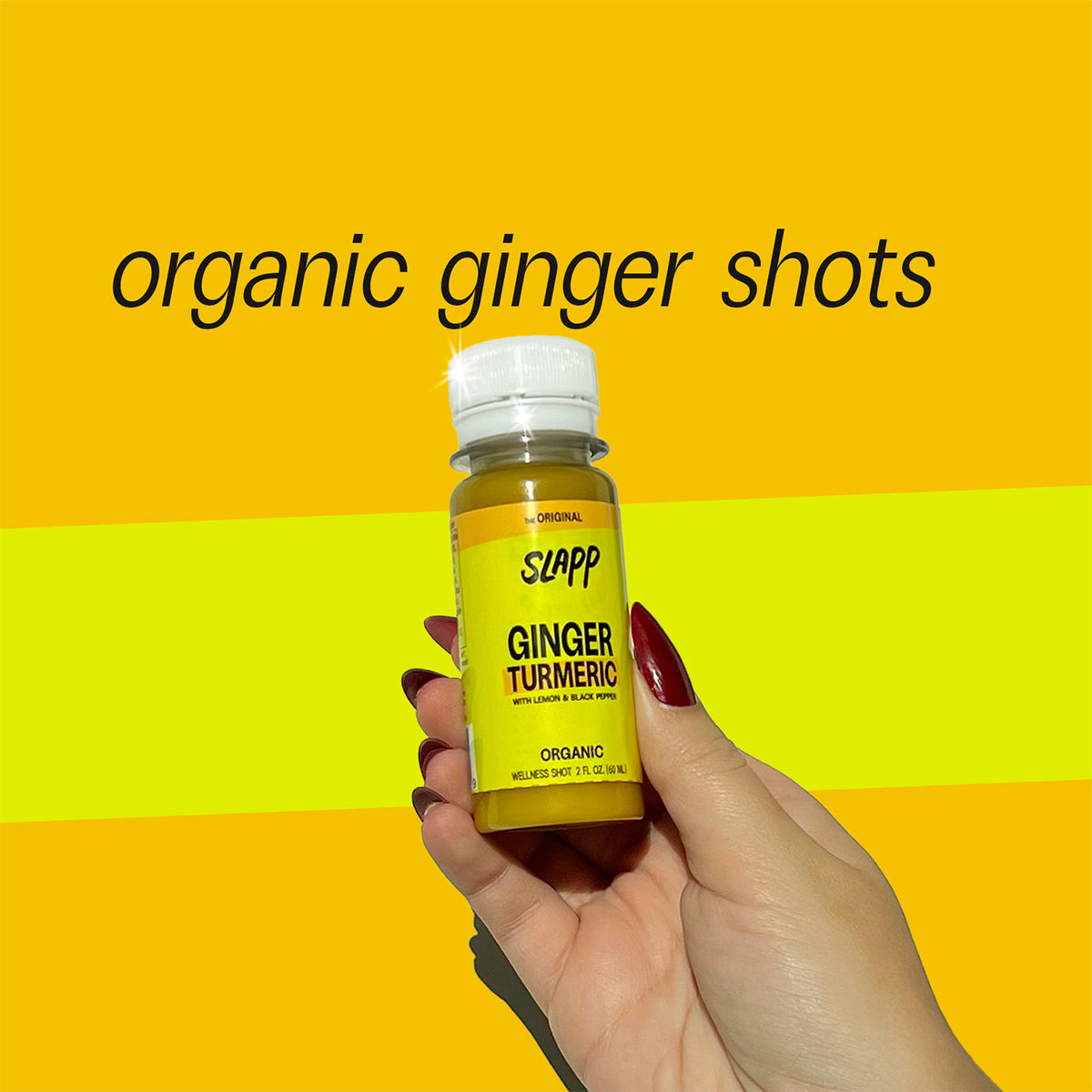 Hand holding a Slapp Ginger Turmeric organic wellness shot bottle with bold yellow background and text that reads - organic ginger shots.