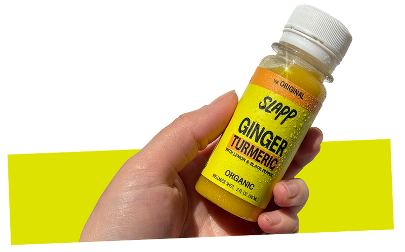 Hand holding a bottle of Slapp Ginger Turmeric wellness shot.